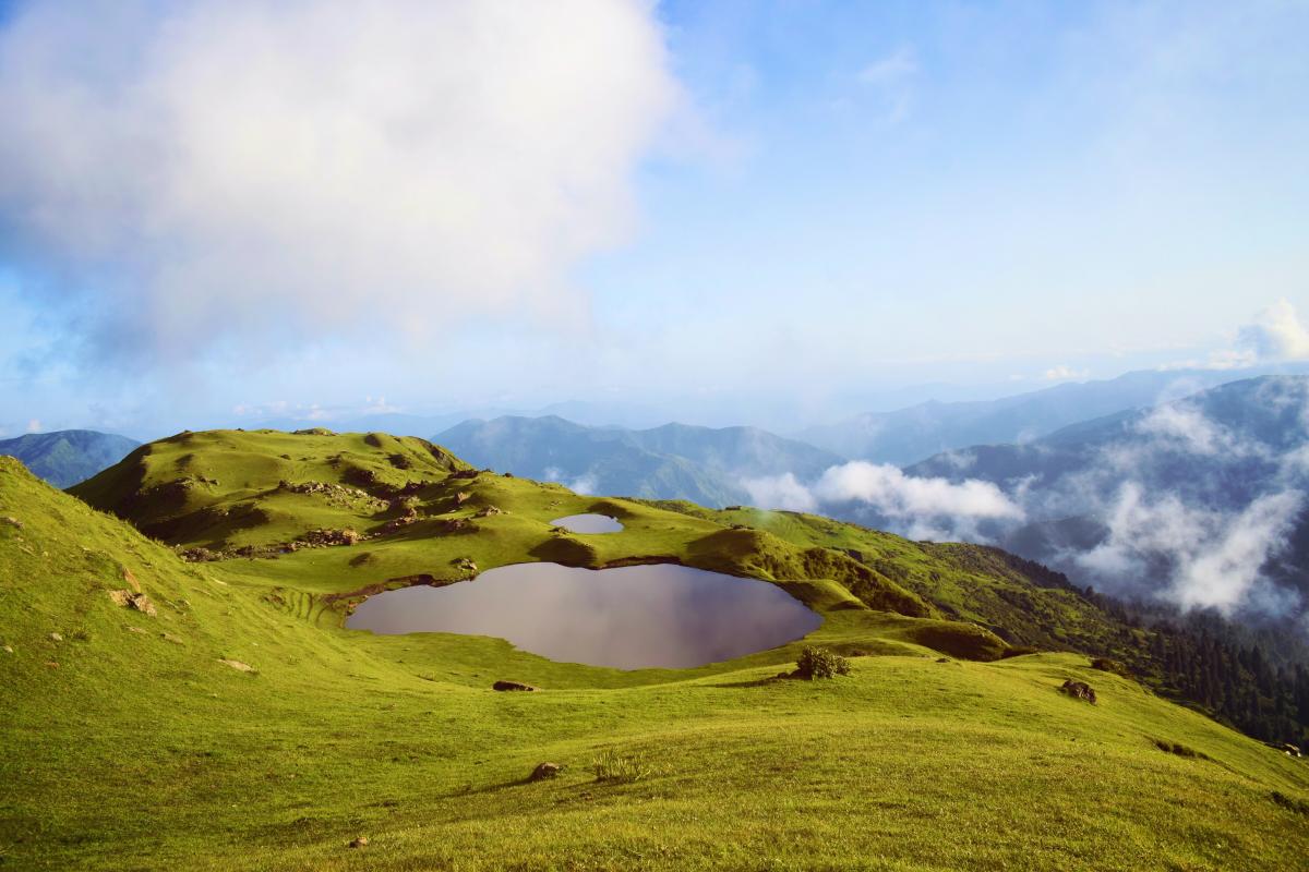 Mountains with a small pond inside of it with larger mountains in the background and cloudy skies above.