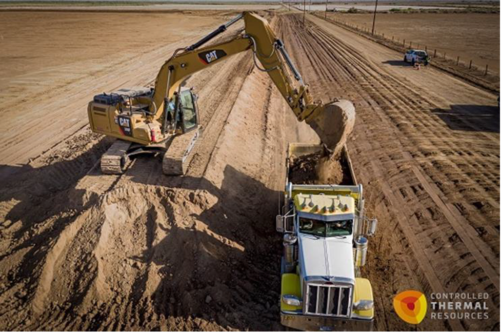 Yellow backhoe loading dirt into dump truck as geothermal pipeline is being constructed