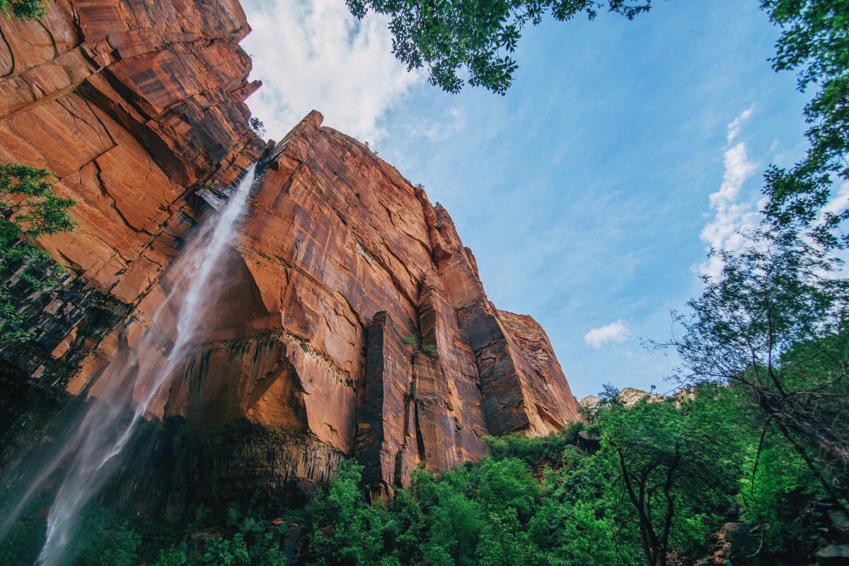 Waterfall coming from tall orange rocks above green trees