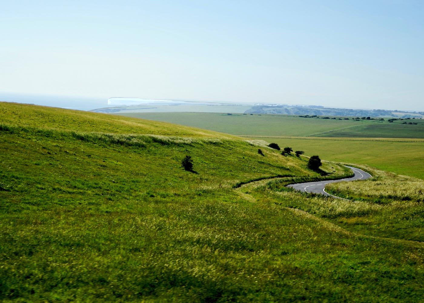 A vast green plane with a winding road going through it and a hazy blue sky.