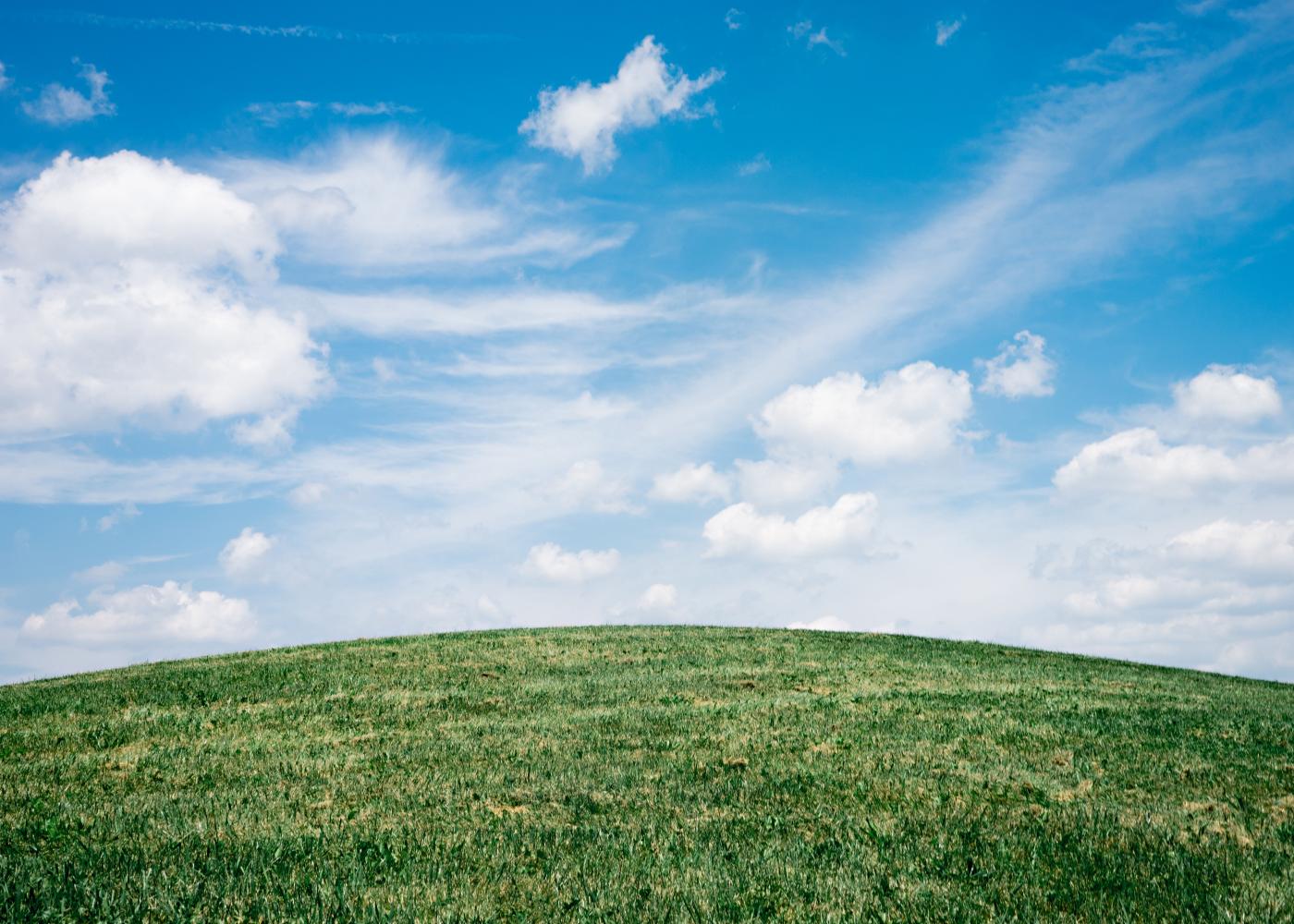 A grassy green knoll with slightly cloudy blue skies above.