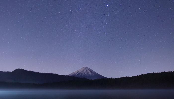 A lake at nighttime with a starry sky and a mountain in the background.