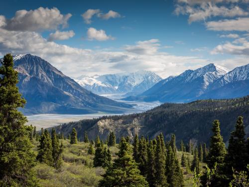 A mountainous region with multiple peaks and valleys, lush greenery, and blue skies