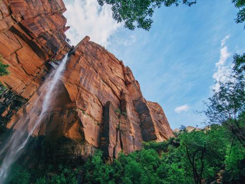 Waterfall coming from tall orange rocks above green trees